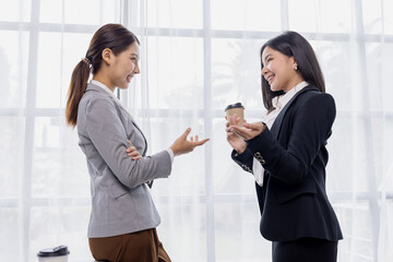 Happy two Asian women standing in suit talking together in the office or workplace, 