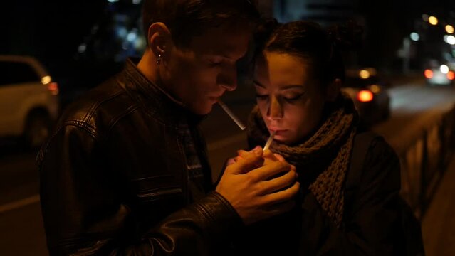Couple in love smoking cigarettes on the street at night. A man and a woman keep warm while smoking cigarettes.