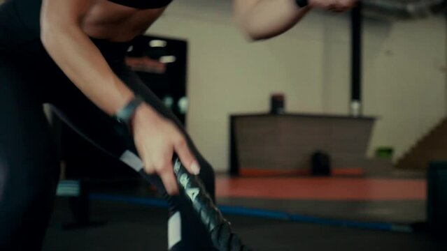 The athlete makes exercises with a rope. A girl in the gym trains. Sexy young woman is engaged in simulators in the gym. Beautiful sport figure.