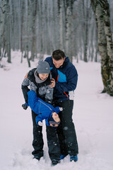 Fototapeta na wymiar Dad hugging mom holding little baby upside down in winter forest