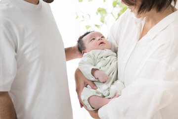 Obraz premium 明るい白い部屋で赤ちゃんを抱っこするお父さんとお母さんの幸せそうな家族顔無し 不妊治療や高齢出産などののイメージ