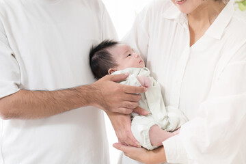 明るい白い部屋で赤ちゃんを抱っこするお父さんとお母さんの幸せそうな家族顔無し　不妊治療や高齢出産などののイメージ