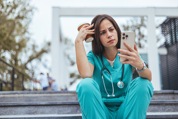 Tired depressed female scrub nurse wears face mask blue uniform gloves sits on hospital stairs...