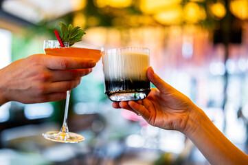 hands of man and women holding and clinking glasses cocktails in restaurant