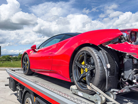 Crashed red Ferrari on a tow truck in sunshine with blue sky and white clouds