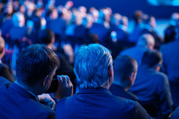 Businessmen listening to speaker giving presentation in illuminated auditorium at export forum 