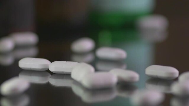 White pills dropping on a table surface, close up. 