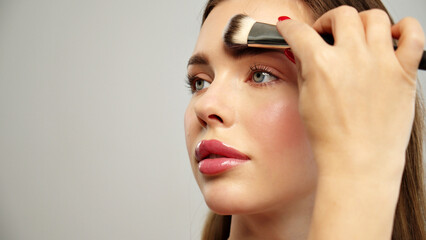 Makeup artist or stylist applies eyeshadow powder or shadows to the eyelids of the female model....
