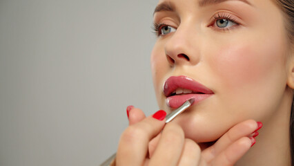 Makeup artist or stylist applies lipstick  to the lips of the female model. Visagiste making make...