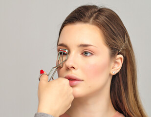 Visagiste curling eyelashes using eyelash curler.  Make-up artist in  studio doing makeup for...