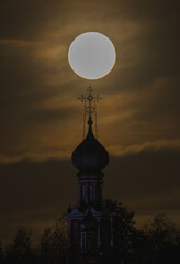 A big yellow moon shines over the church