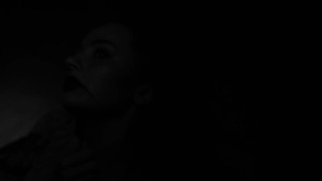 Brunette girl in Halloween style. A woman on a black background, a flickering light on her face, a scary scene. Terrible darkness. Depression, suffering, crime. Black Carnival, in the basement.