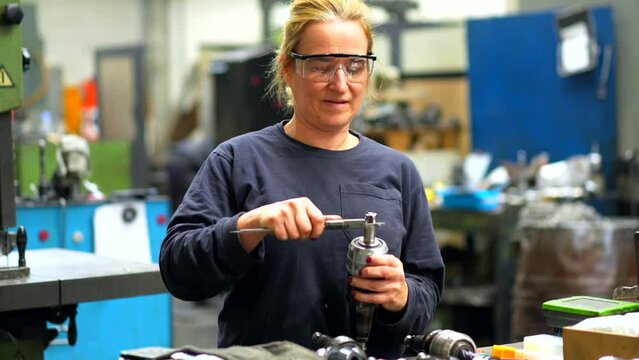 Female factory worker operator working in numerical control sector measuring drill bits, industrial factory