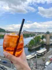 hand holds glass of cocktail over river and prague city view in Czech republic