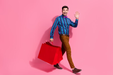 Full length photo of charismatic funny guy steps with red gift packages bags black friday model wave palm isolated on pink color background