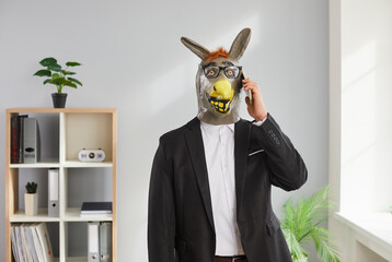 Portrait of a funny man in a suit and white shirt wearing animal donkey mask on head standing in...
