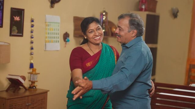 Happy Indian senior coupes dancing together by holding hands at home - concept of freedom, retirement lifestyle and entertainment