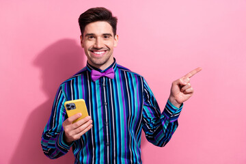 Photo of elegant charismatic guy toothy smile hold smart phone indicate finger empty space isolated...