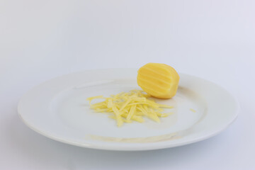 A miniature grater and grated potatoes on a white plate.