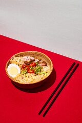 Asian culture, cuisine. Delicious recipes. Plate with noodles, egg and meet, served with greenery isolated red background.