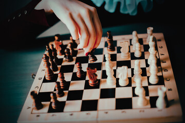 The hand of an elegant woman in a vintage jabot rearranges wooden chess pieces on a chessboard. A...