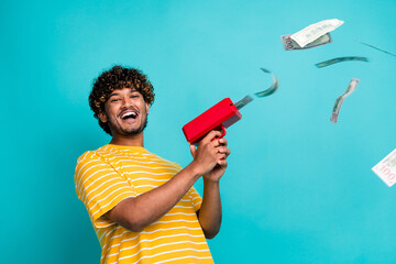 Photo of overjoyed successful guy hold money gun shooting flying dollar bills isolated on teal color background