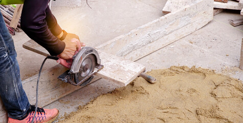 Construction builder worker uses a circular saw to cut wood at building site for preparation to...