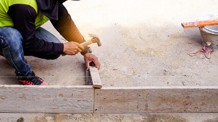 Construction builder worker uses a hammer to driving iron nail into a wooden beam at building site...