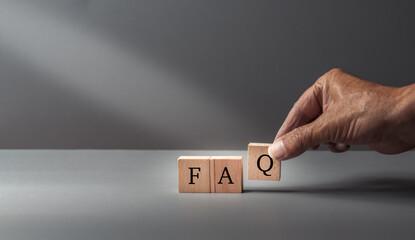 hand posing FAQ, frequently asked questions, text FAQ, written on wooden cubes on  a grey blue...