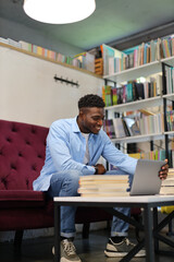 Young African American student with a laptop, studying in a modern library, blending technology and education.