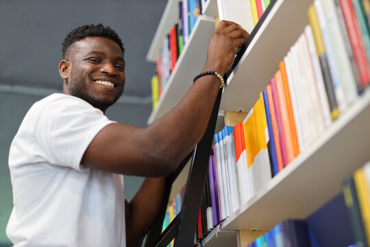 A focused young man in a university library, surrounded by books, representing academic dedication and intellectual pursuit.