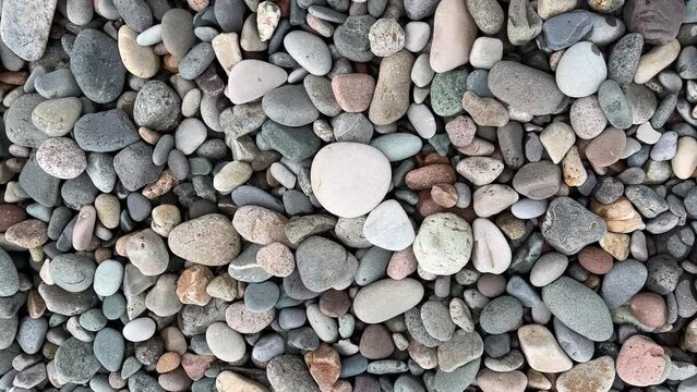 4K horizontal video. Pebble beach. Background with gray, white, pink stones on seashore. Concept of summer holidays, ocean travel, tourism, vacation. Shore. View from above. Top view. Georgia. Texture