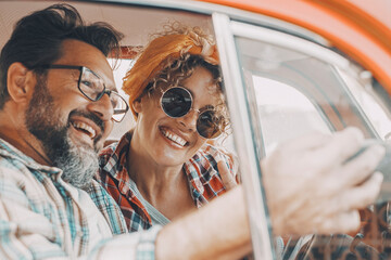 Happy couple having fun inside a car during travel adventure. Cheerful man and woman smiling and laughing a lot together. People enjoying vehicle trip in friendship and relationship. Concept of drive - obrazy, fototapety, plakaty