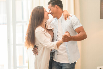 Interracial couple dance at home together having fun and love. New house owner and loan leisure indoor activity. Boy and girl in relationship have fun at home dancing and smiling to each other