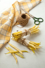 Several pods and two bunch of flat runner bean pods heap with yellow kitchen towel, scissors and ball of thread on wooden white background. .