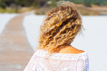 Back view of blonde surf waves hairstyle woman enjoying the beach in summer holiday vacation. Concept of tourist and tourism in the nature. Female people walking on the sand outdoor