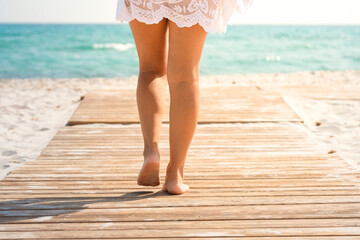 Back view of beautiful woman legs walking in summer on a wooden pier at the beach. Tropical summer...