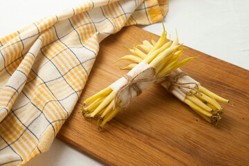 Cutting board with two bunches of flat runner bean pods heap, yellow kitchen towel on white wooden...