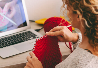 Woman at home doing knit work watching online tutorial class lesson on laptop computer online. Modern work female people activity with internet connection. Wooleen yarn knitting hobby indoor