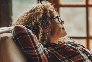 Adult middle age woman stretch and relax at home sitting on the chair looking outside the windows...