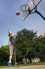 Cute boy in gray t shirt plays basketball on city playground.