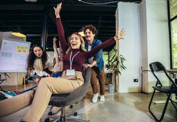 Fototapeta na wymiar Young cheerful businesspeople in smart casual wear having fun while racing on office chairs and smiling