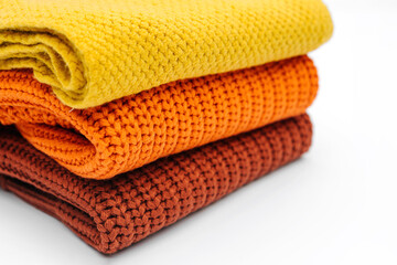 Stack of knitted sweaters and scarf  on white background. Women's warm jumpers, stylish autumn or winter clothes. Fashion autumnal outfit. Cozy bright  fall look.