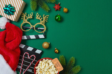 Christmas movie night and party concept with  popcorn, Santa hat, decorations and movie clapper board on green background. Top view, flat lay - obrazy, fototapety, plakaty