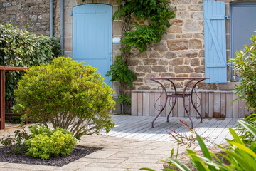 Terrasse en bois et salon de jardin au pied d'une maison en pierre.