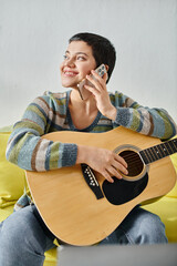 vertical shot of cheerful woman with piercing holding guitar and talking by phone, education at home