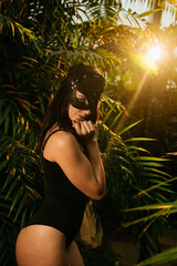Sexy woman in a BDSM cat mask posing in a tropical garden among palm trees. BDSM concept.