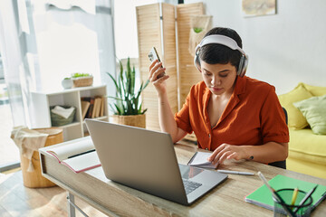 young woman checking her notes while studying with phone in hands and laptop on table, education