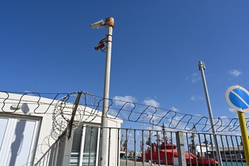 The barbed wire on top of the fence and CCTV cameras at the entrance of passenger dock. The fence...