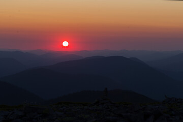 Silhouettes of Carpathian mountains in a natural blue-red gradient with the sun in the middle. Carpathians at sunrise with silhouettes of ridges and peaks. Gorgany, Carpathians, Ukraine.